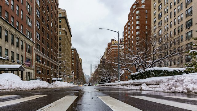 A snowy New York avenue lined with brick apartment buildings in winter